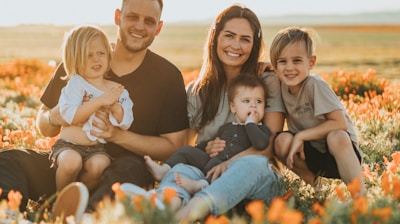 3 women and 2 men sitting on green grass field during daytime